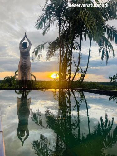 a person standing next to a swimming pool with the sunset at Reserva Natural Natura Park in Puerto Nariño
