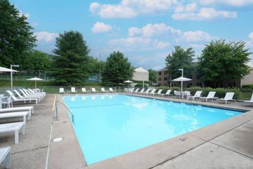 une grande piscine avec des chaises longues blanches et des parasols dans l'établissement Modern 1 BR APT w/ Pool, Tennis court, Wi-Fi, & AC, à Monroeville