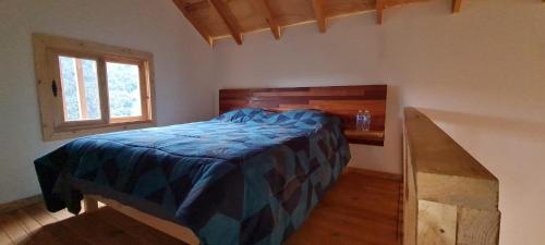 a bedroom with a bed with a blue comforter and a window at Colibri - Cabañas Puerto del Zopilote in Pinal de Amoles