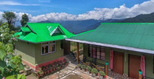 a house with a green roof with mountains in the background at 3 Sisters' Homestay in Ravangla