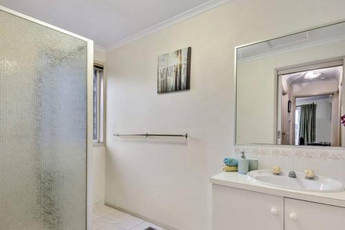 a white bathroom with a sink and a mirror at Corner Cottage in Dandenong