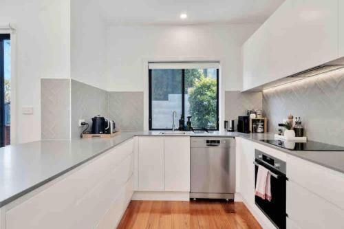 a white kitchen with a sink and a window at Spacious modern 3 bdr home minutes from beach in Merewether