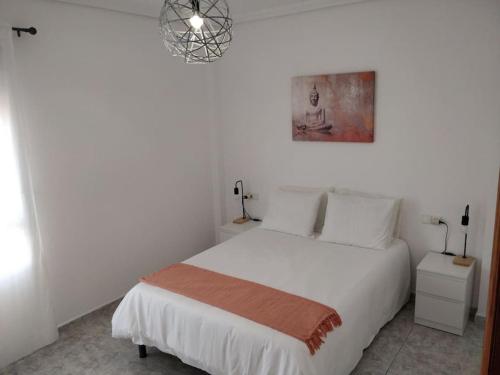a bedroom with a white bed and a chandelier at VV 'TIRBA' Precioso duplex a 1 minuto de la playa in Gran Tarajal