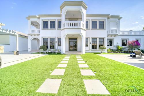 a large white house with a green lawn at Signature 6BR Villa with Assistant Room and Private Pool in Frond F Palm Jumeirah by Deluxe Holiday Homes in Dubai