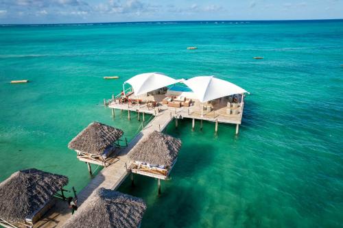 a pier with tables and umbrellas in the water at Blue Moon Resort in Jambiani