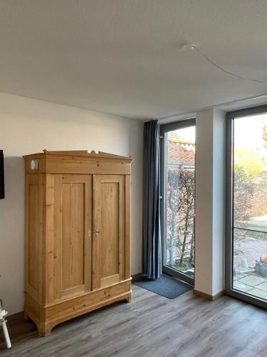 a room with a wooden cabinet and two windows at Kapitänshaus mit Hafenblick in Greetsiel