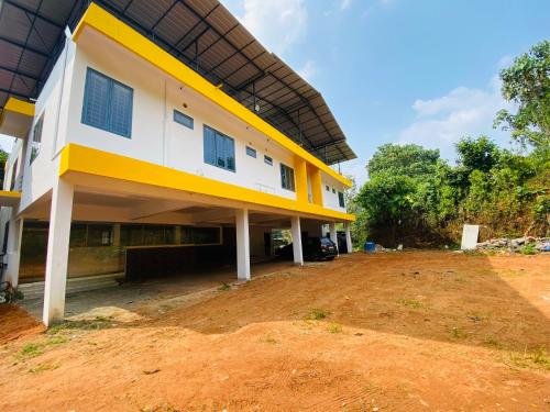 un bâtiment jaune et blanc avec une cour en terre dans l'établissement Erumely Central Homes, à Mundakāyam