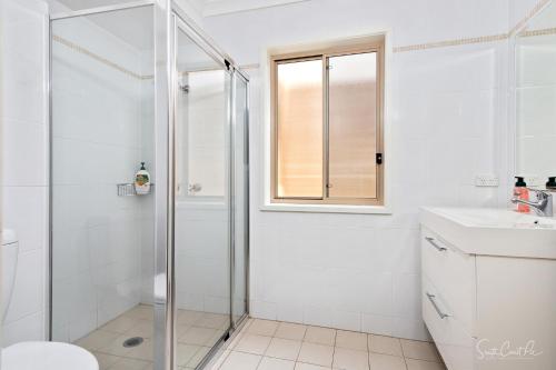a white bathroom with a shower and a sink at Parker by the Sea in Batemans Bay