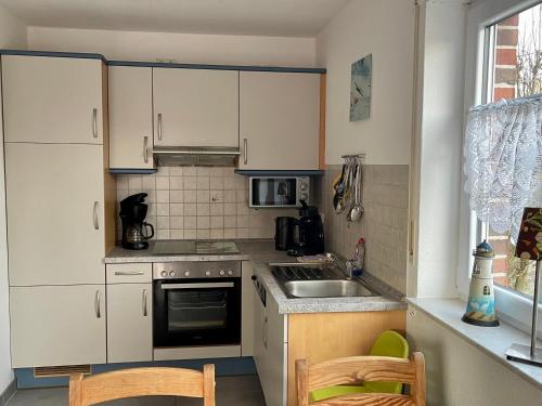 een kleine keuken met witte kasten en een wastafel bij Ferienhaus Seehund in Krummhörn
