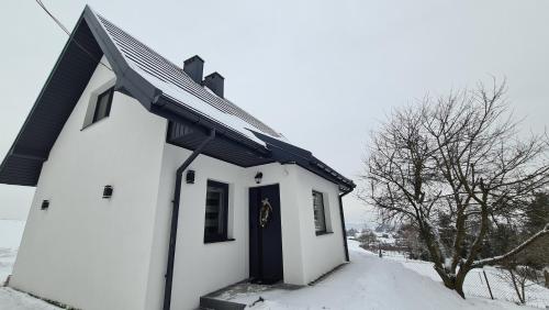 a small white building with a blue door in the snow at Domek pod Wiśnią in Mizerna