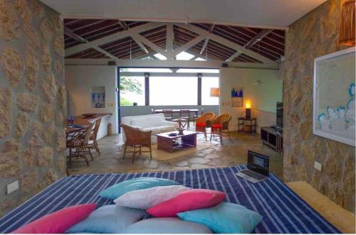 a bedroom with a bed with pillows and a living room at Sítio Promontório - Casa Grécia in Ubatuba