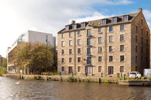 a large brick building next to a river at Lovely 2 Bedroom B-listed converted Whisky bond in Edinburgh