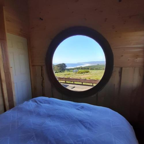 a round window in a wooden cabin with a bed at PUESTA DE SOL in Cobquecura