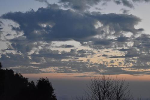 a cloudy sky at sunset with trees in the foreground at Bagar Trails in Nainital