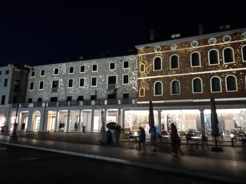 - un bâtiment avec des personnes marchant devant lui la nuit dans l'établissement IL VICOLO_Carinissimo appartamento in centro storico, zona giorno mansardata, à Belluno