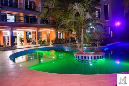 a swimming pool with a palm tree in front of a building at Mendiata Hotel in Accra