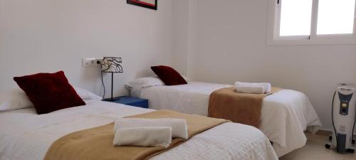 a room with three beds with white sheets and red pillows at Apartamento TomCar Piscina, Pádel, wifi y zonas comunes in Sanlúcar de Barrameda