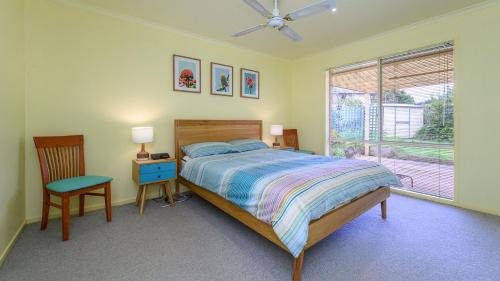 a bedroom with a bed and a chair and a window at Serrell by the Sea in Inverloch