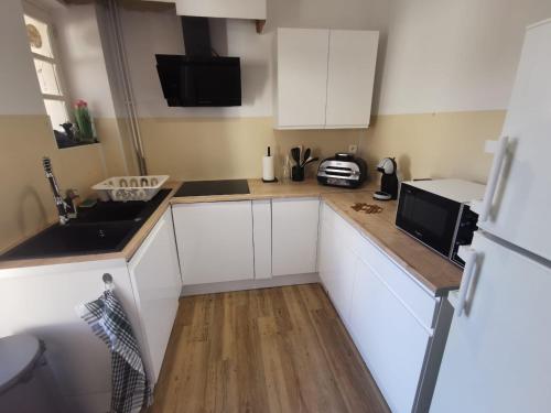 une cuisine avec des armoires blanches, un évier et un réfrigérateur dans l'établissement La Coquette Albigeoise - Maison Albi centre rénovée - WIFI - Vue - Jardin, à Albi