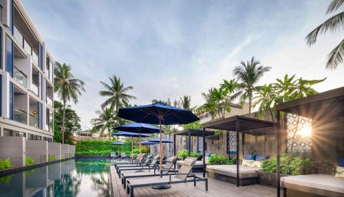 einen Pool mit Stühlen und Sonnenschirmen neben einem Gebäude in der Unterkunft Hotel Indigo Phuket Patong, an IHG Hotel in Patong Beach