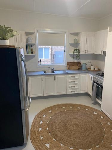 a kitchen with white cabinets and a black refrigerator at Stay Salty in Culburra Beach