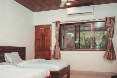 a bedroom with two beds and a window with curtains at Anant Resort Nagaon Beach Walking Distance 2min Alibaug in Alibaug