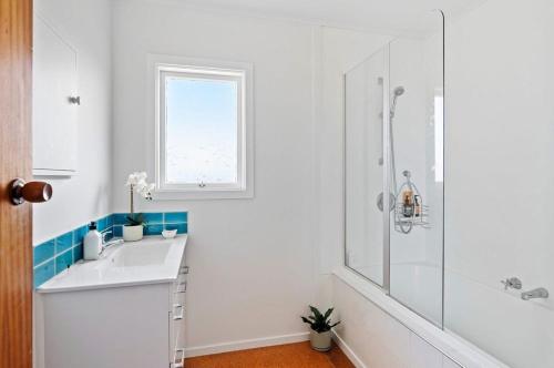 ein weißes Bad mit einem Waschbecken und einer Dusche in der Unterkunft Emily's Beach House - Kaiteriteri Holiday Home in Kaiteriteri