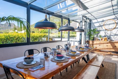 a dining room with a table and chairs and windows at Hout & About Guest House in Hout Bay