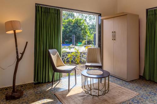 a room with two chairs and a table and a large window at SaffronStays Apricus Farm, Karjat in Karjat