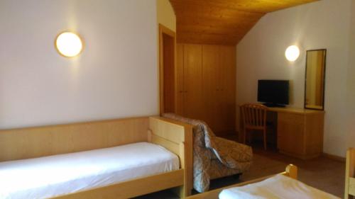 a room with two beds and a desk and a tv at Hotel Casa Alpina - Alpin Haus in Selva di Val Gardena