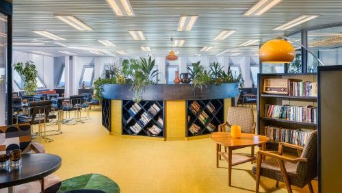 a library with bookshelves and tables and plants at Brown Brut Seafront Hotel, a member of Brown Hotels in Tel Aviv