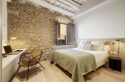 - une chambre avec un mur en pierre, un lit et un bureau dans l'établissement Canvas Apartments & Lofts Girona, à Gérone