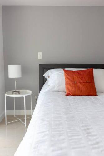 a white bed with a red pillow and a side table at Sunshine Ocean and City Views 1 BR Paradise with Parking in Miami