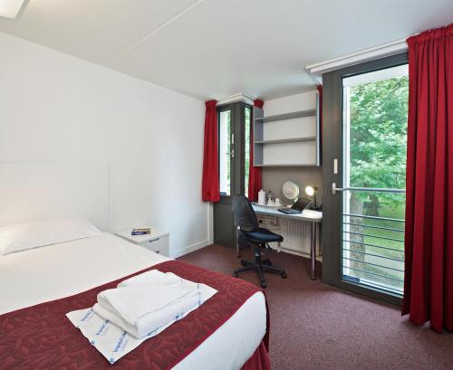 ロンドンにあるプリンシズ ガーデンズのベッド、デスク、窓が備わるホテルルームです。