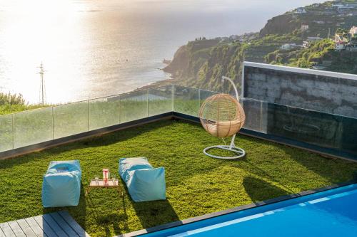 a balcony with a rattan chair and chairs on the grass at Villa Candelária by An Island Apart in Ribeira Brava