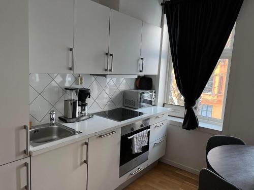 een keuken met witte kasten, een wastafel en een raam bij Fløyen Apartment in Bergen