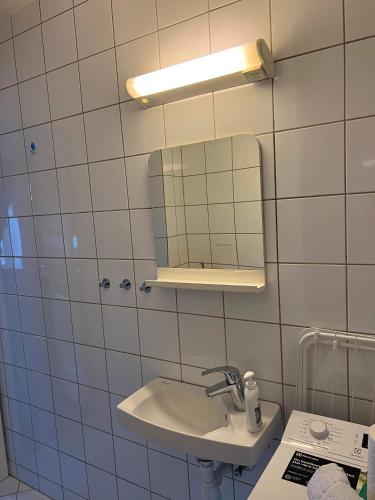 een wit betegelde badkamer met een wastafel en een spiegel bij Fløyen Apartment in Bergen