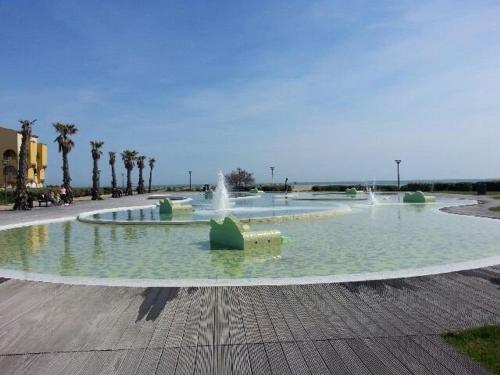 une grande fontaine dans un parc planté de palmiers dans l'établissement Maison T2 à Port Leucate, face à la mer, 4 couchages, parking privé, TV, lave-linge, commerces à 400m - FR-1-81-55, à Port-Leucate