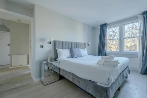 a bedroom with a large white bed with blue curtains at Modern and Luxurious 2 Bedroom Flat - Barons Court in London