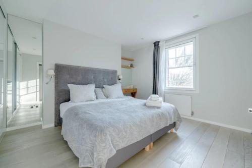 a white bedroom with a large bed and a window at Modern and Luxurious 2 Bedroom Flat - Barons Court in London