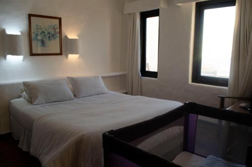 a bedroom with a bed with white sheets and two windows at Club Hotel Casapueblo in Punta del Este
