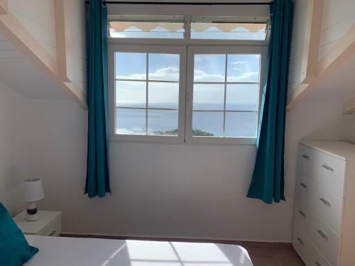 a bedroom with a window with blue curtains at PARADIS AU SOLEIL, vue panoramique sur mer in Bouillante