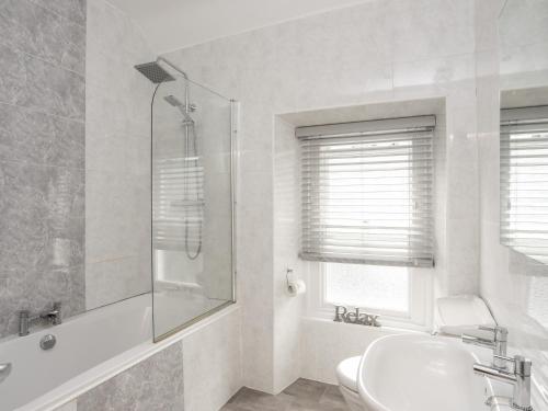 a white bathroom with a shower and a sink at 6 Erasmus Street in Penmaen-mawr