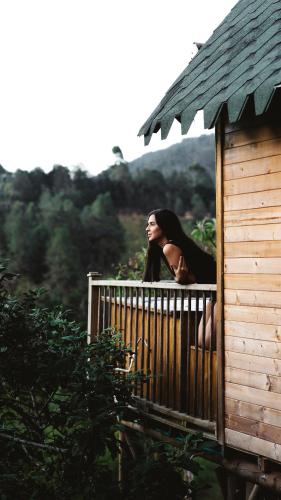 a woman sitting on a balcony of a wooden building at Guané Glamping Ecolodge Jacuzzi Privado Oriente Antioqueño in Guarne
