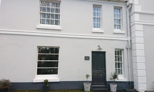 a white house with a black door and two potted plants at Lincombe Court Apartment Wellswood Torquay in Torquay