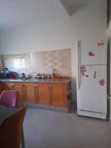a kitchen with a white refrigerator and wooden cabinets at Appartement ennasr49 in Khenifra
