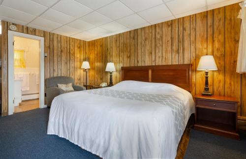 Schlafzimmer mit einem großen weißen Bett und Holzwänden in der Unterkunft Knob Hill Motor Lodge in Hillsville