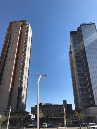 two tall buildings in a parking lot with a blue sky at Urban Awe Apartment: iTowers 21st Floor in Gaborone
