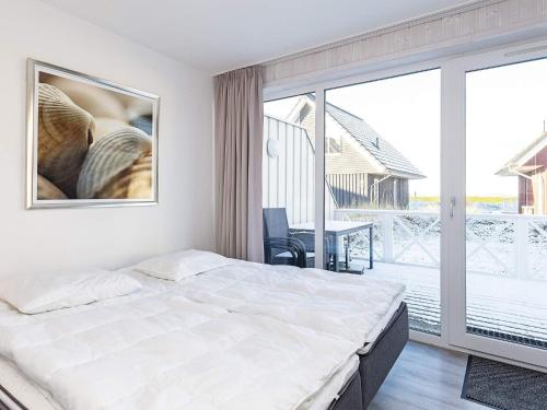 a white bedroom with a bed and a balcony at Holiday Home Strandblick IV in Wendtorf