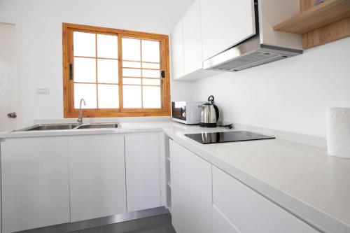 eine weiße Küche mit einem Waschbecken und einem Fenster in der Unterkunft Villa Sunrise Garden A181 in Ban Muang Mai